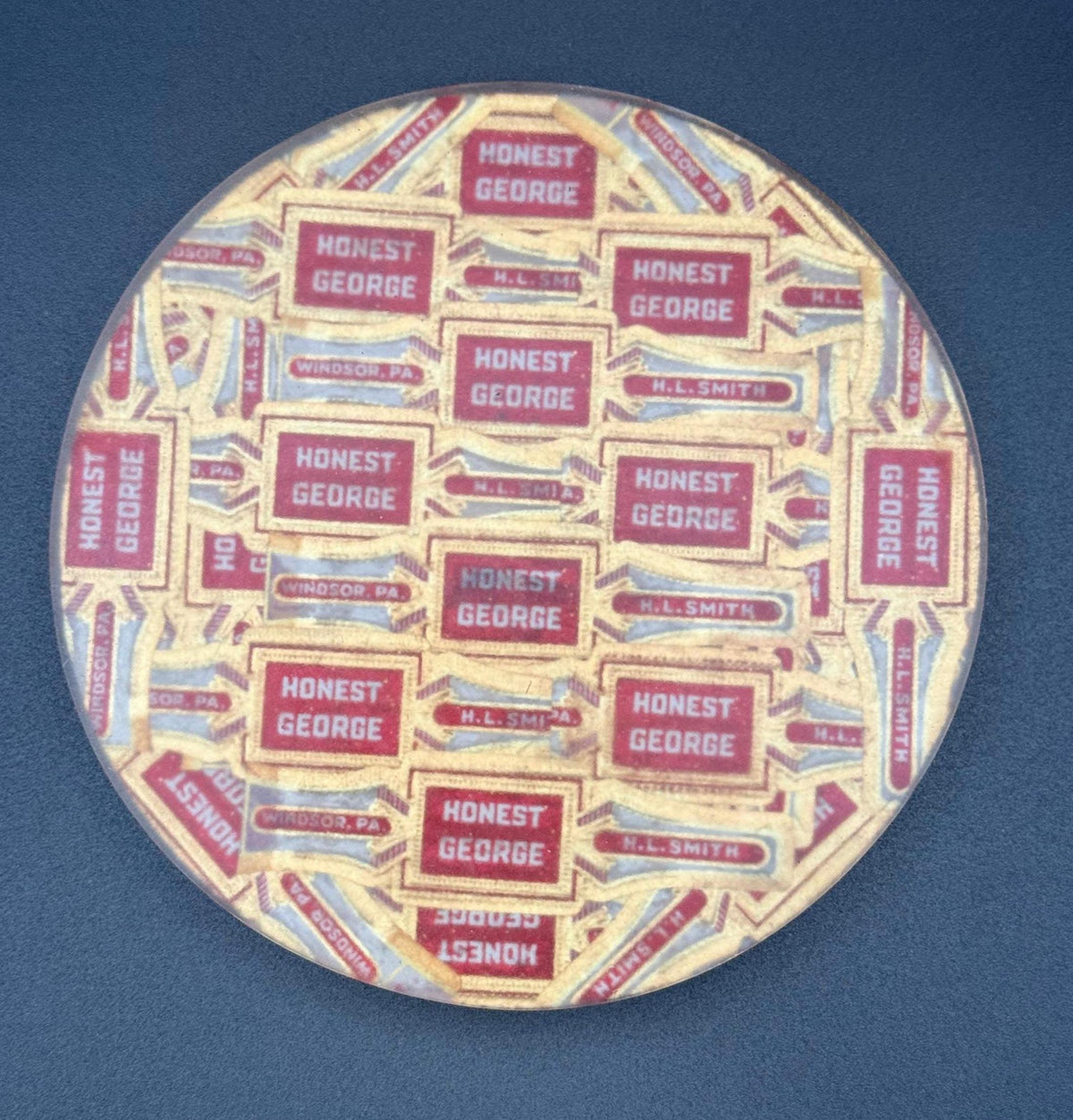 May include: Round coaster featuring a repeating pattern of "HONEST GEORGE" text in red boxes on a beige background. The text "H.L. SMITH" and "WINDSOR, PA" are also visible. The coaster has a clear protective coating.vintage cigar, cigar coasters, cigar box art, antique cigar, whiskey coaster, bar drink coaster, cigar lounge decor, man cave decor, epoxy coasters, wood coasters, cigar gift, retro bar decor, classic bar decor